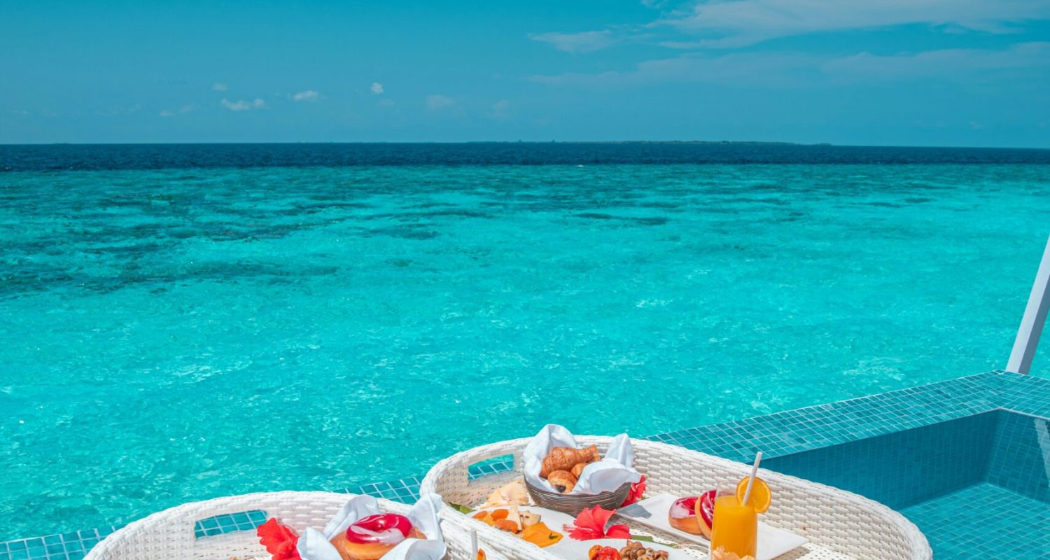 Affordable last-minute beach hotel deals 2025 – infinity pool overlooking turquoise ocean with breakfast trays